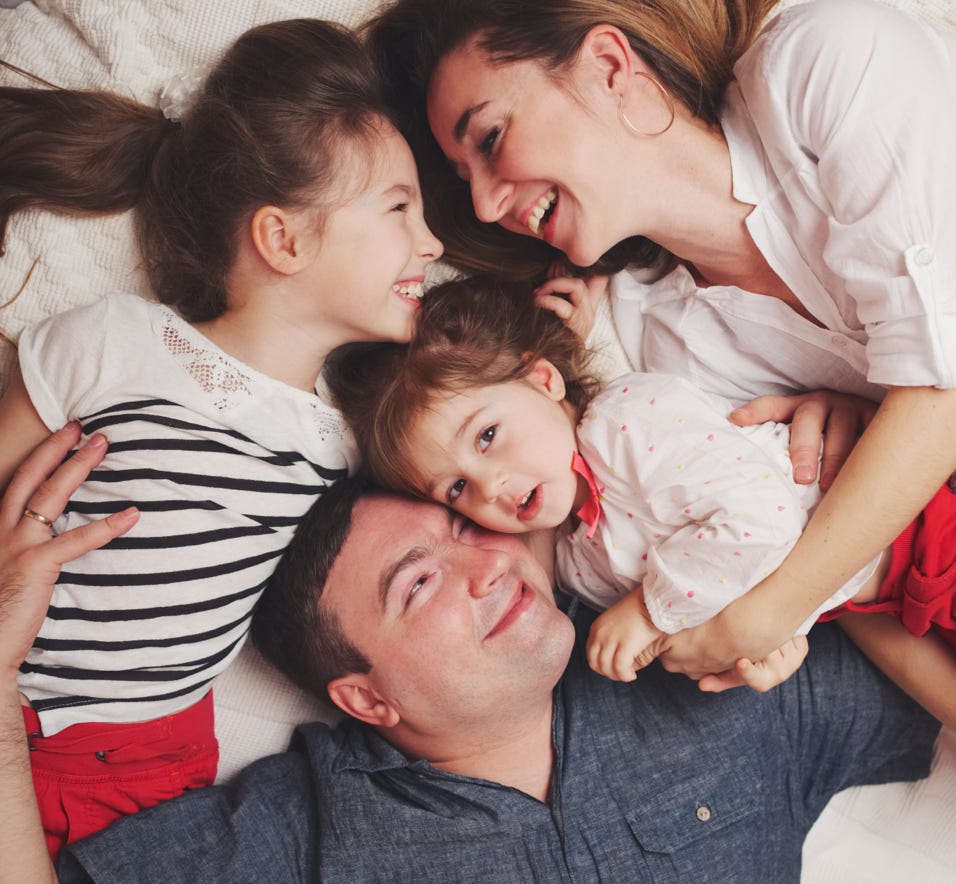 Thema Familie: Vier Personen liegen lächelnd auf einem Bett, zwei Erwachsene und zwei Kinder.